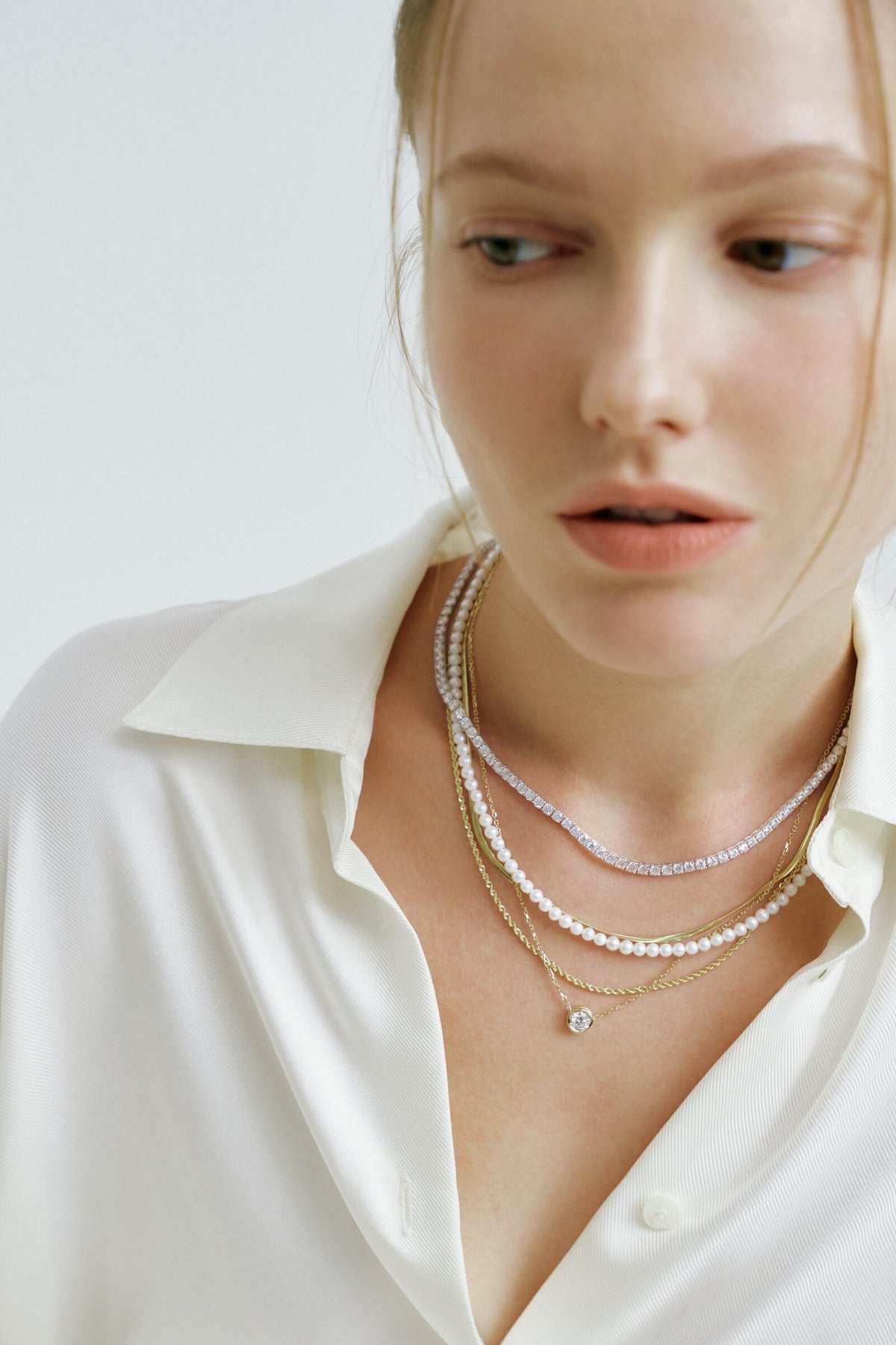 A freshwater pearl strand layered with diamond and gold chains over a white shirt.