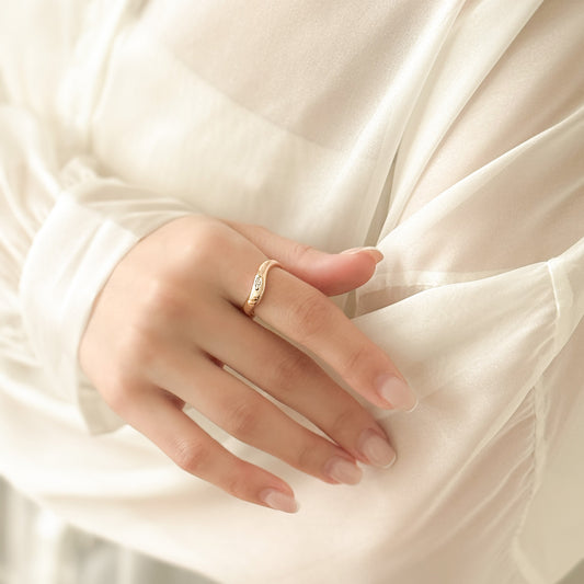 Close-up of a hand wearing a gold ring with a soft, blurred background