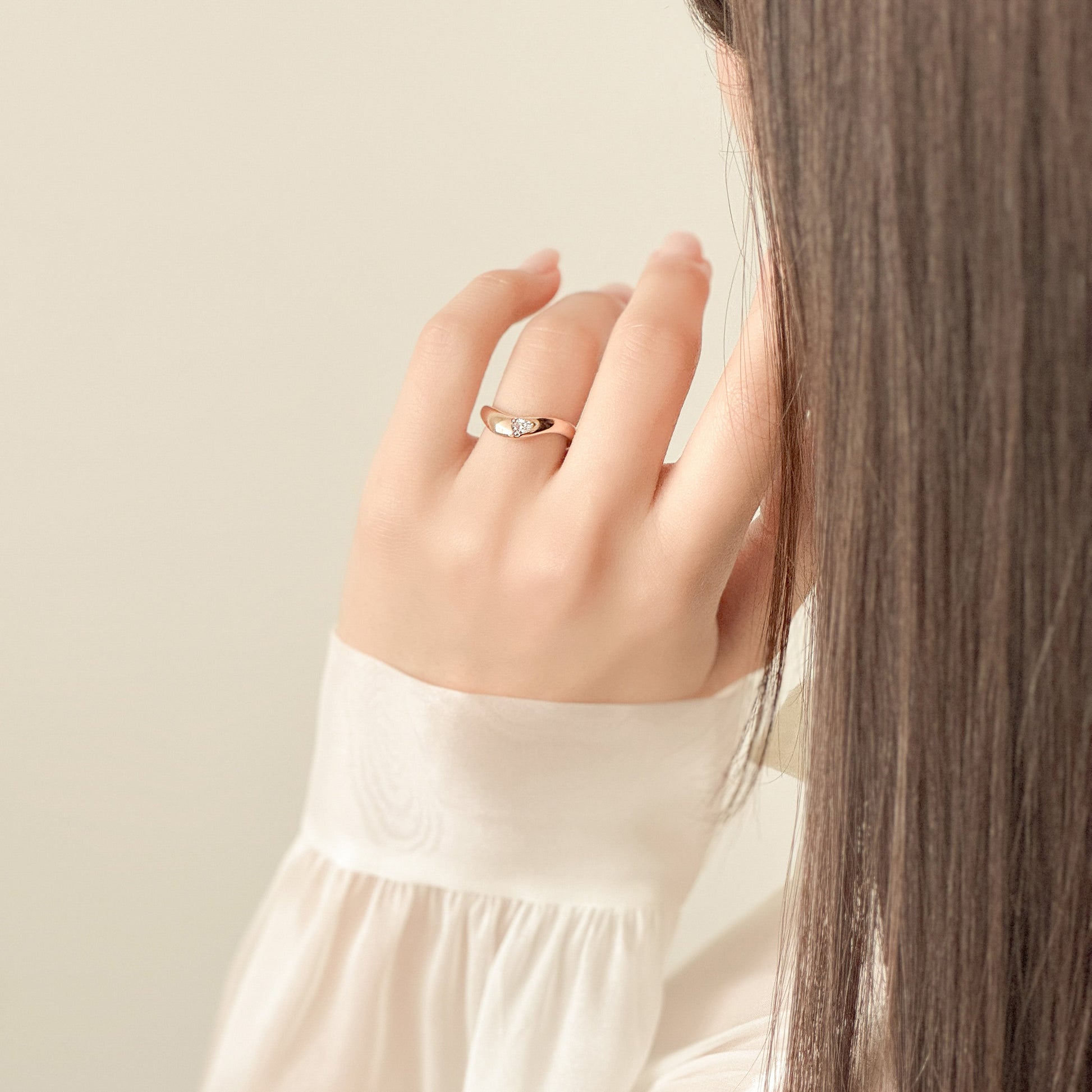 Close-up of a hand wearing a gold ring with a plain background
