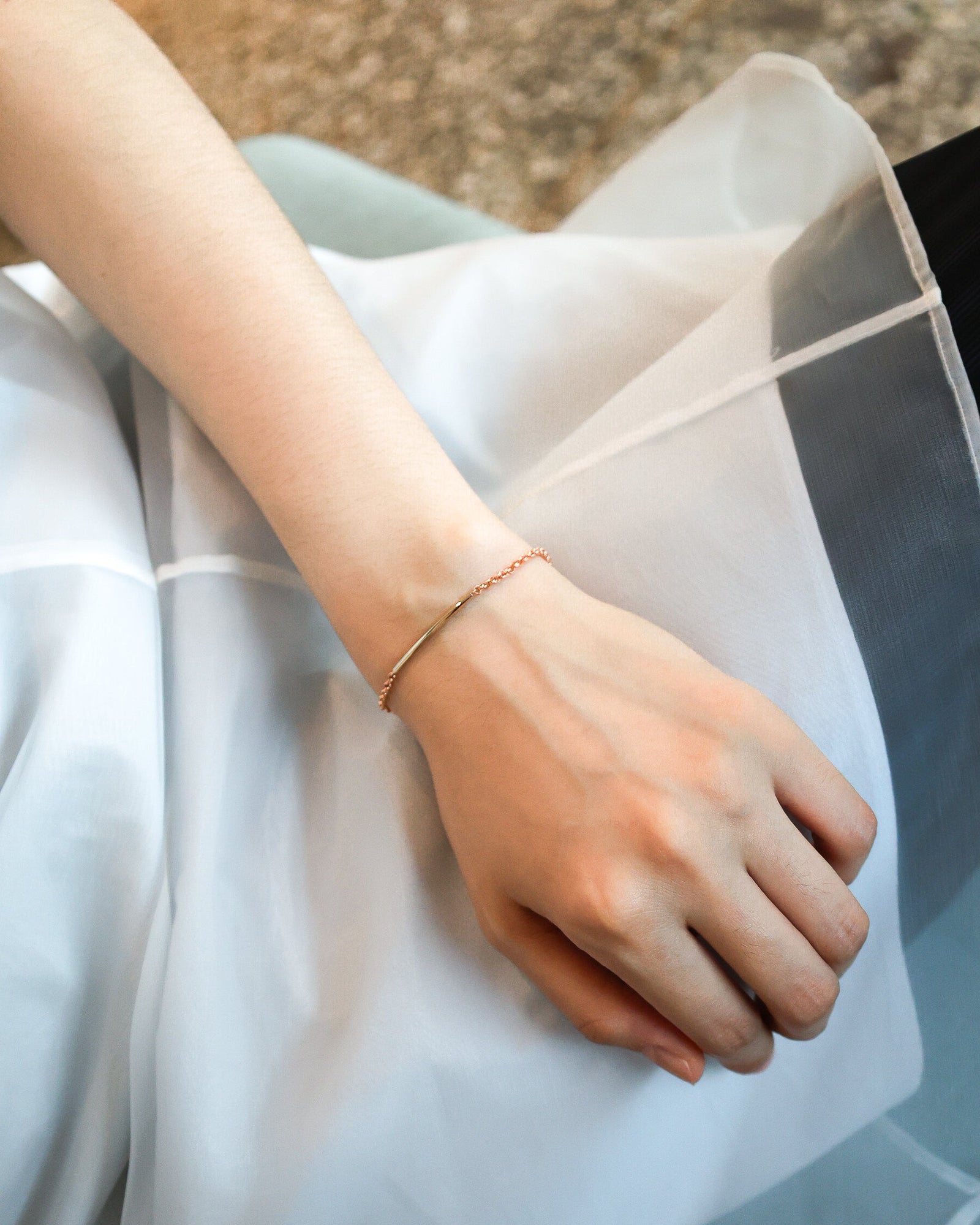 Hand wearing a gold bracelet on a light fabric background