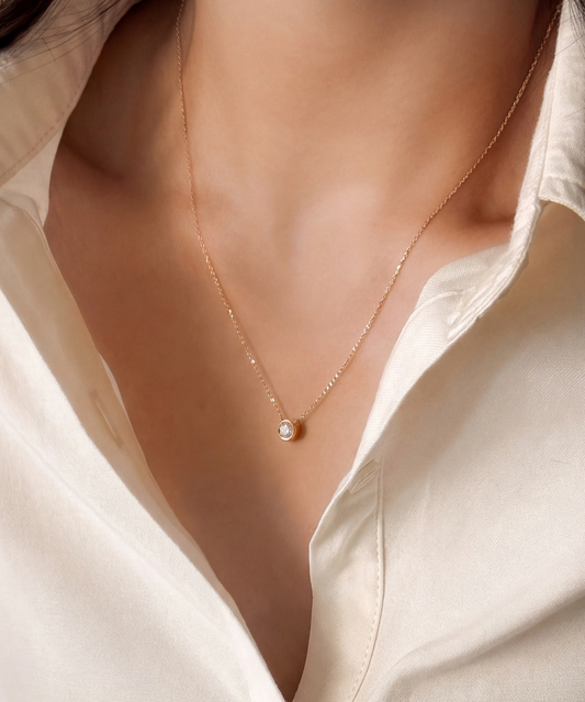 Bezel necklace worn at the collarbone with an open cream shirt, close up