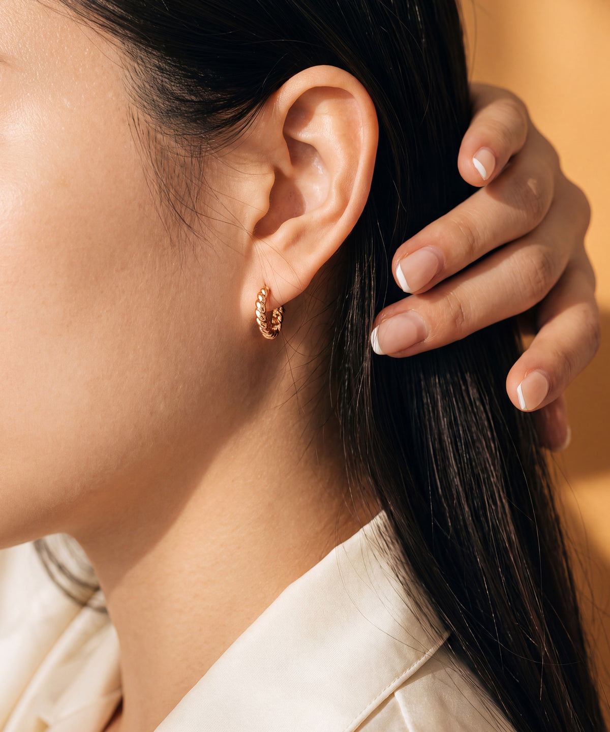 Brioche Hoop Earrings worn, hand in the hair, marigold background