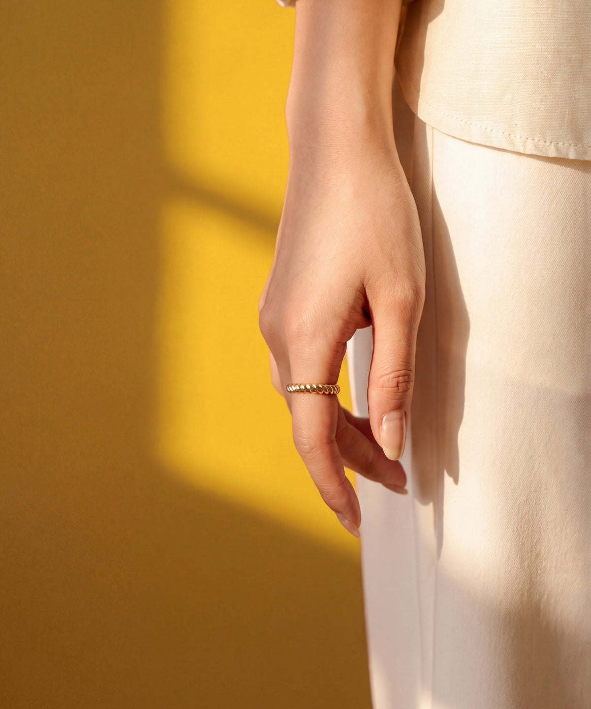 Brioche Ring worn on a relaxed hand against a sunlit marigold wall