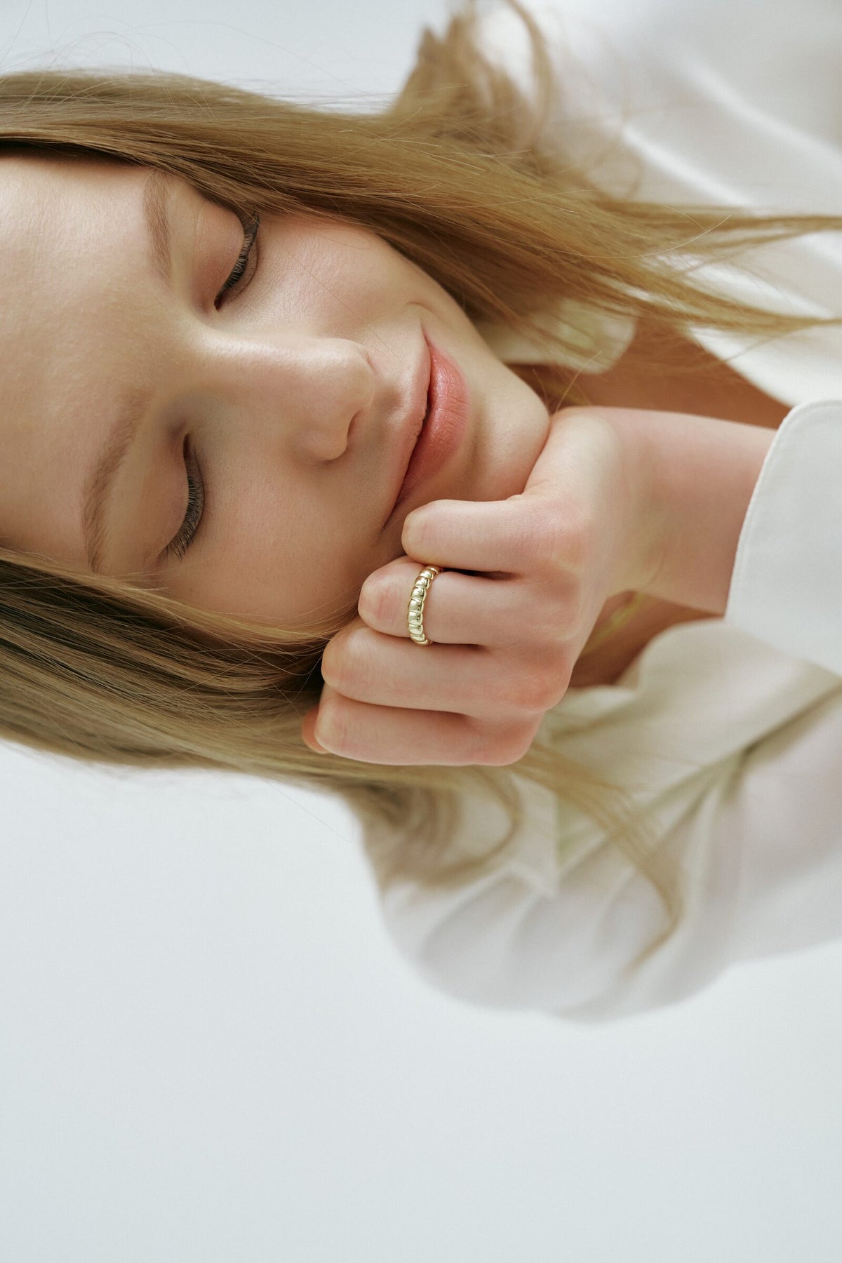 A woman lies on her side with eyes closed and her hand under her chin, a wide segmented ring on one finger.