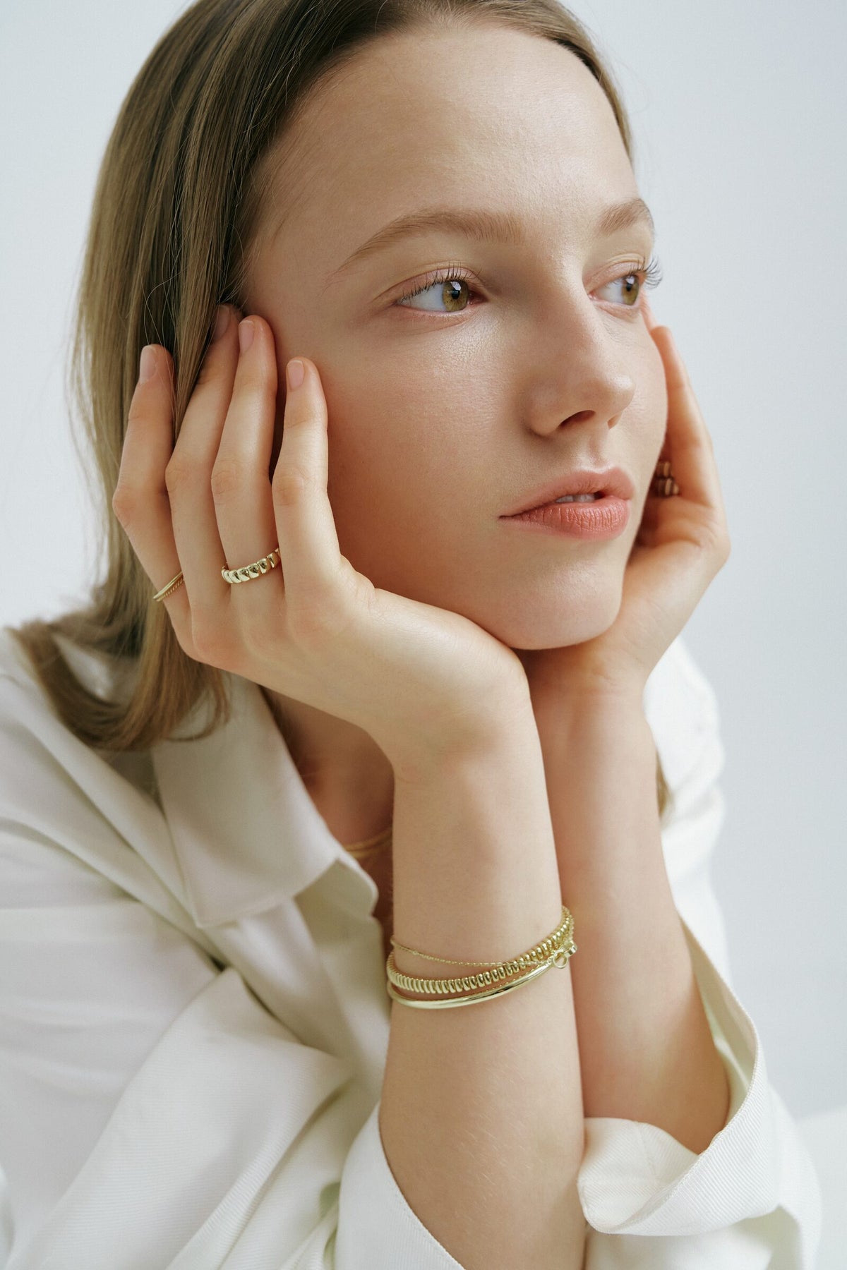 Chin in her hands, a Brioche Ring and a slim band, an Accordion Bracelet and bangle at the wrist.