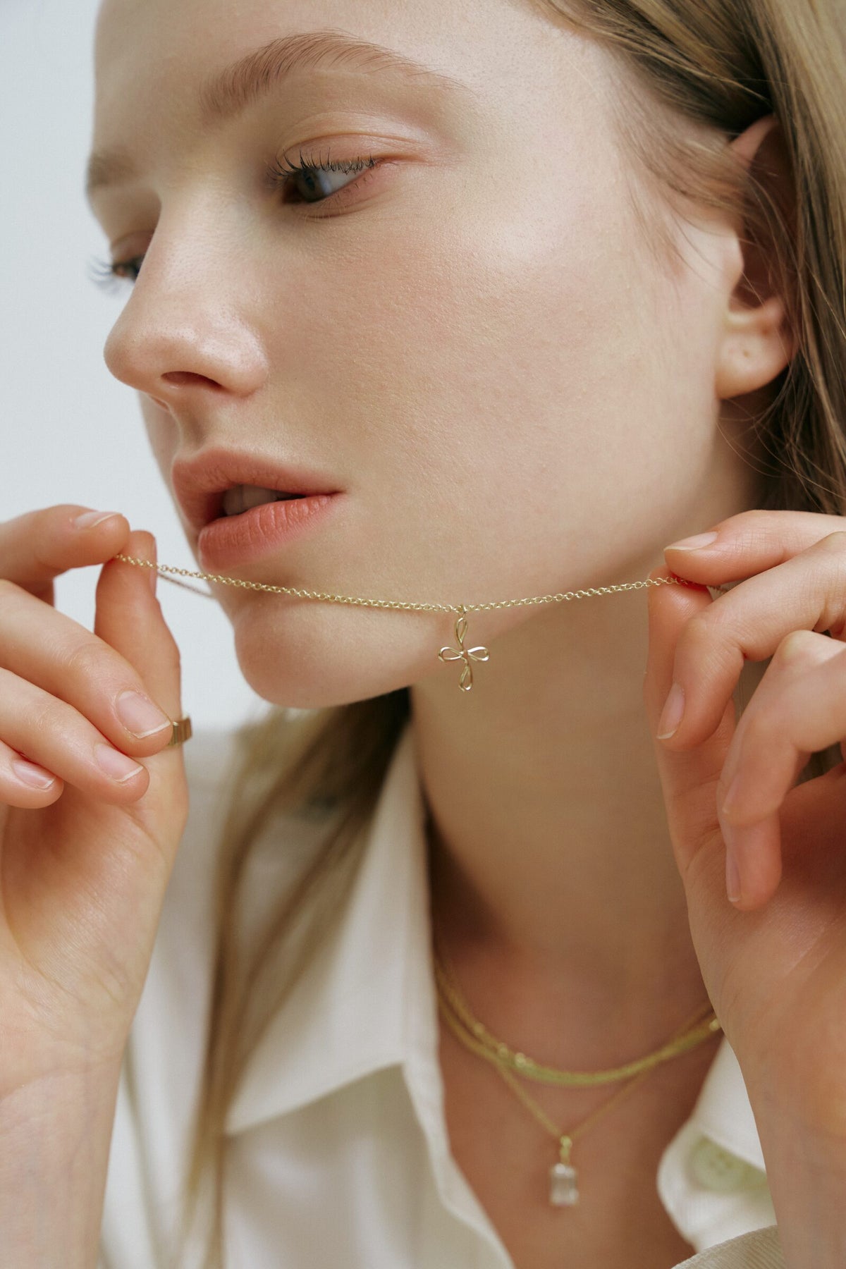 A woman holds a chain with an outlined cross pendant up to her chin, a flat chain and a clear stone pendant at her collar.