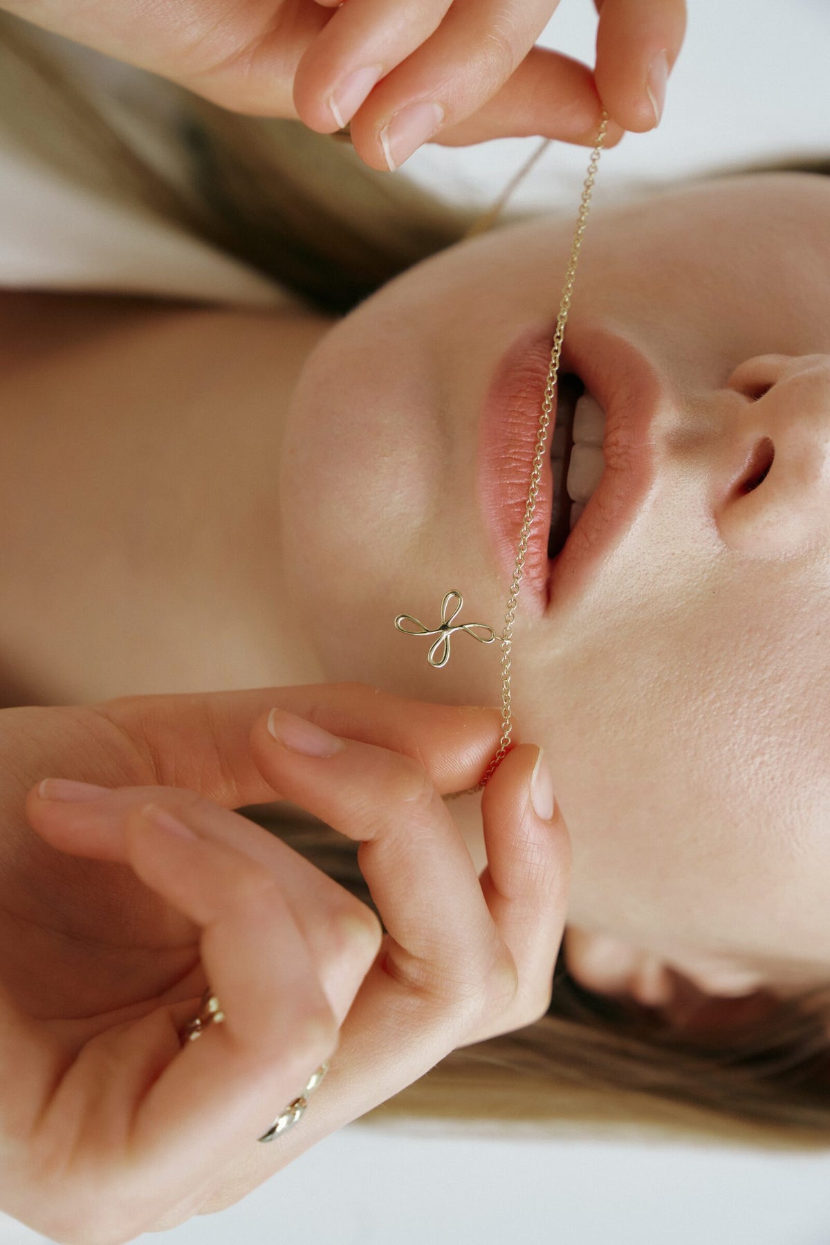 Upside down, the fine chain of the Bloom Necklace held taut across her lips.