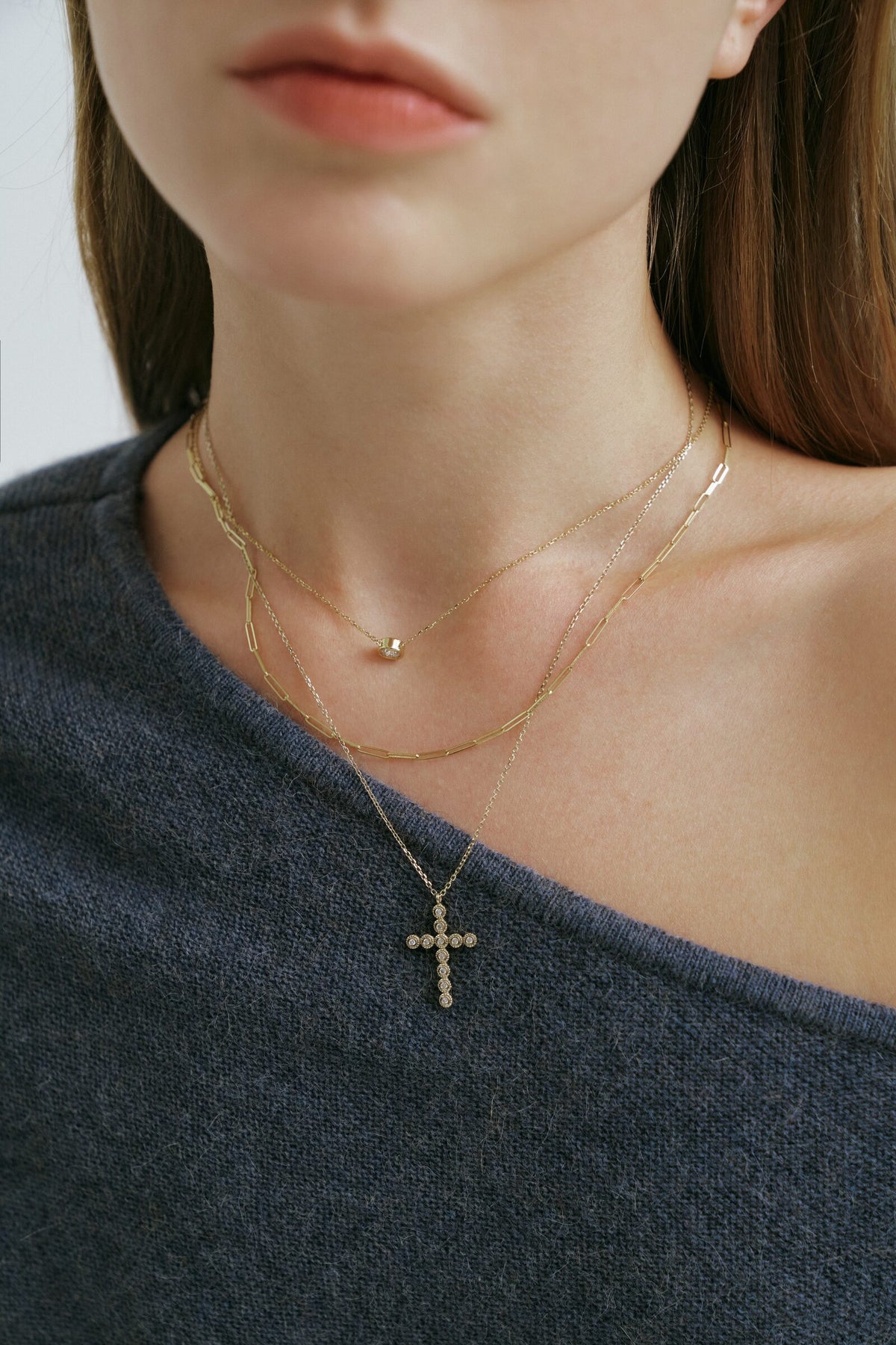 Close crop below the lips, the Bezel Cross Necklace layered with fine chains on a slate knit.