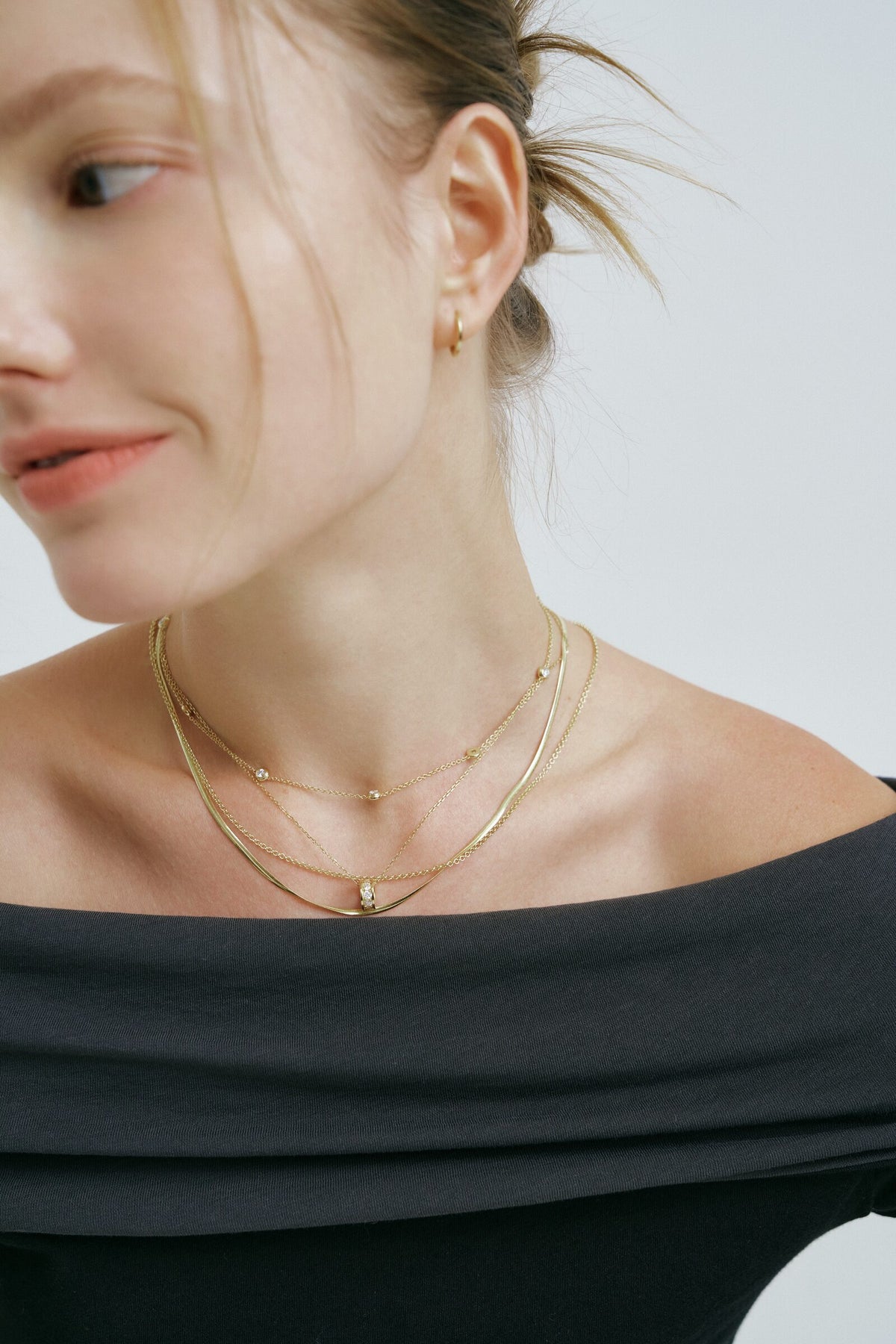 Looking down to the left, the Rondelle Necklace layered with fine chains at the collarbone.