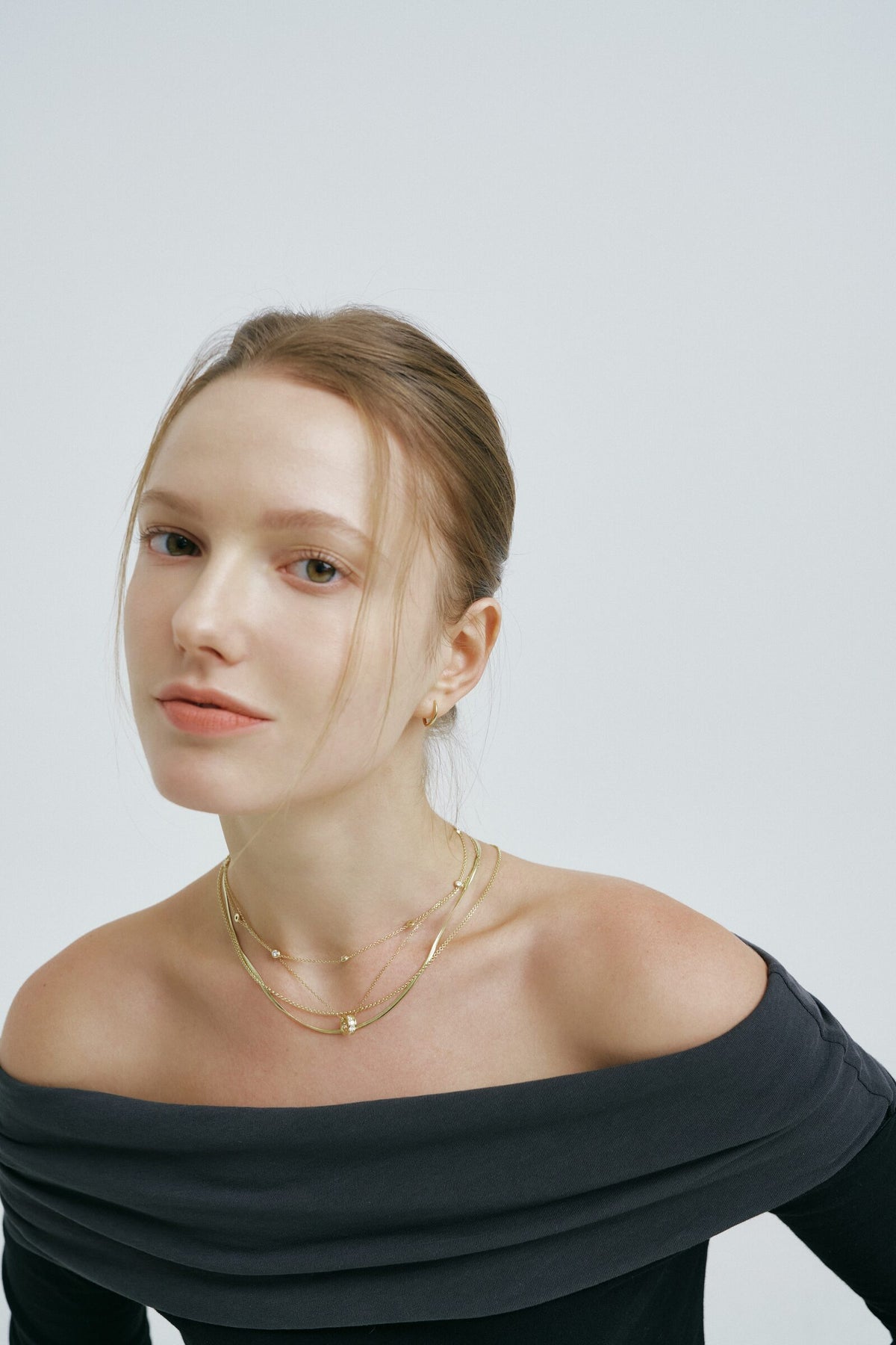 Hair up, charcoal off the shoulder, she meets the camera, the Rondelle Necklace layered at the collarbone.