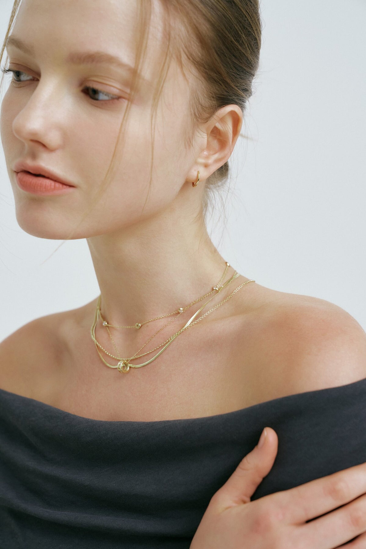 She looks down past her shoulder, the Rondelle Necklace and a herringbone chain at the collarbone.