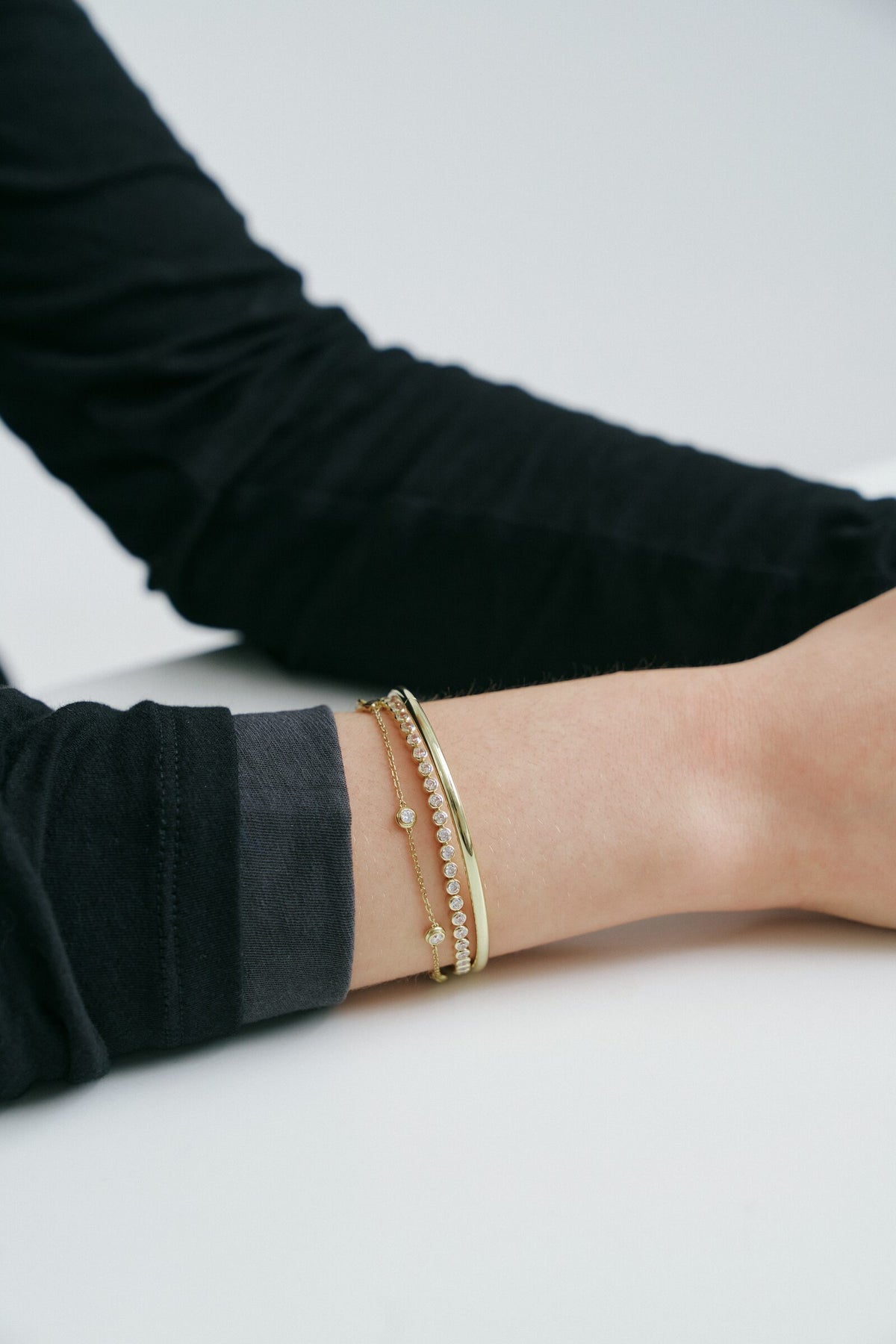 An arm resting on the table, a stack of gold and diamond bracelets at the wrist.