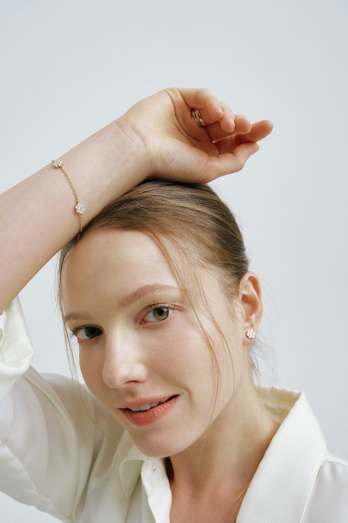 A woman rests an arm on her head and looks at the camera, a bracelet of clear stone flowers and a matching stud earring.