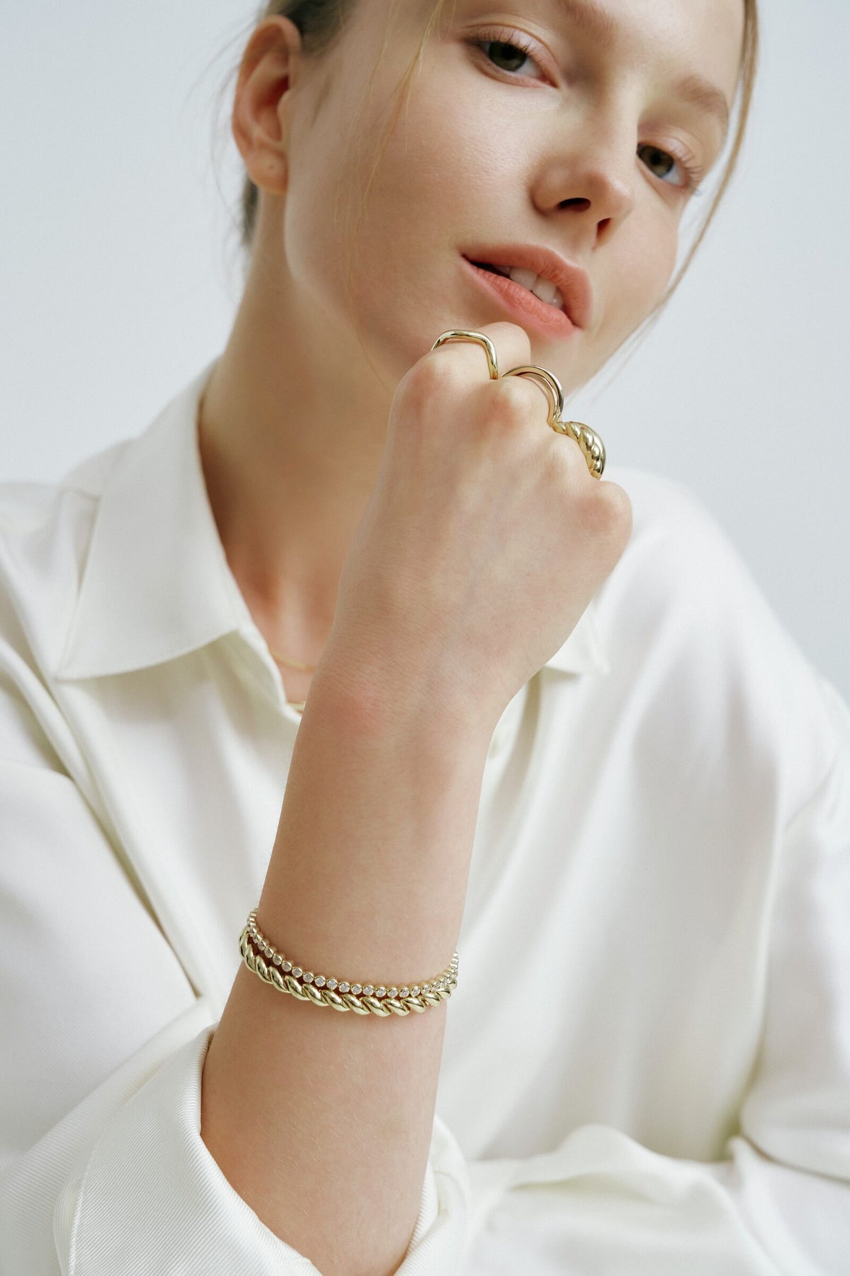 A fist at her chin with a Wave Ring and a Croissant Ring, a twisted rope bracelet and a bezel tennis bracelet at the wrist.