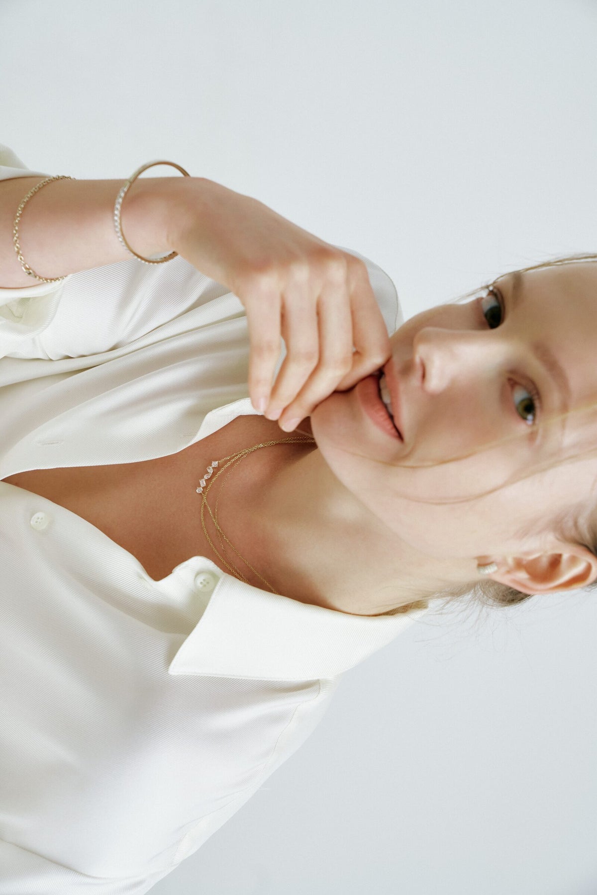 A woman lies back and bites a fingertip, a bangle of clear stones and a chain bracelet, a line of clear stones at her neck.