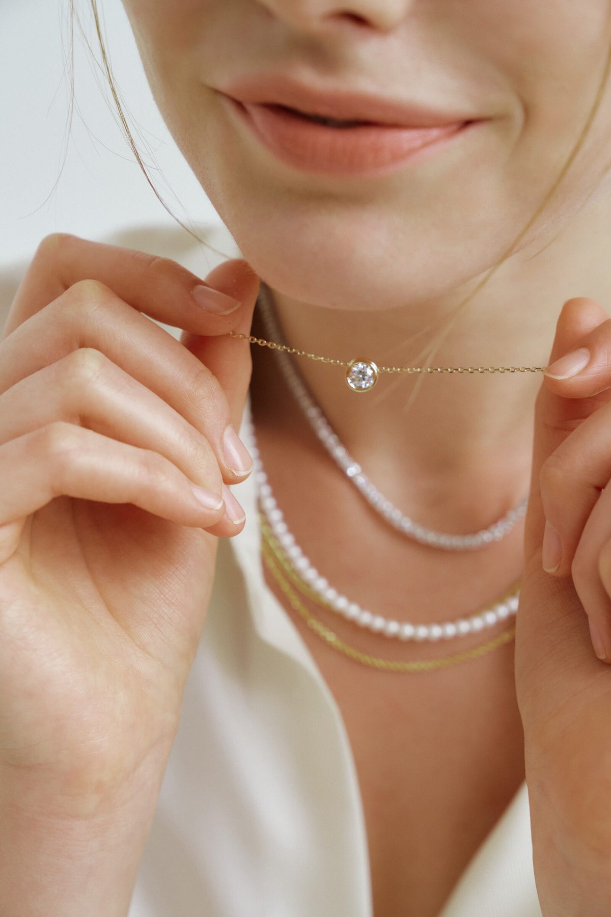 She holds a bezel solitaire out on its chain, pearls and diamonds layered below.