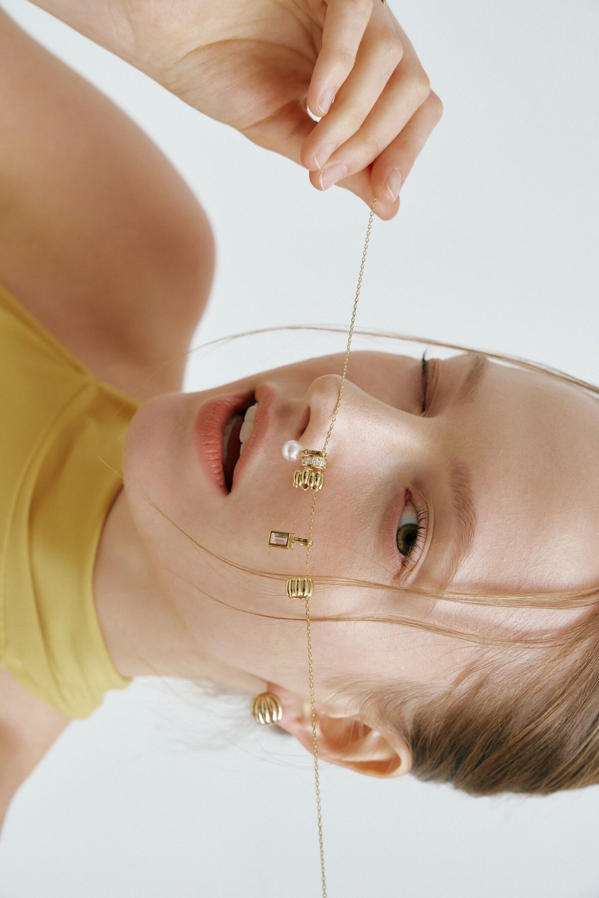 Upside down, a gold charm necklace pulled taut across her face, marigold halter.