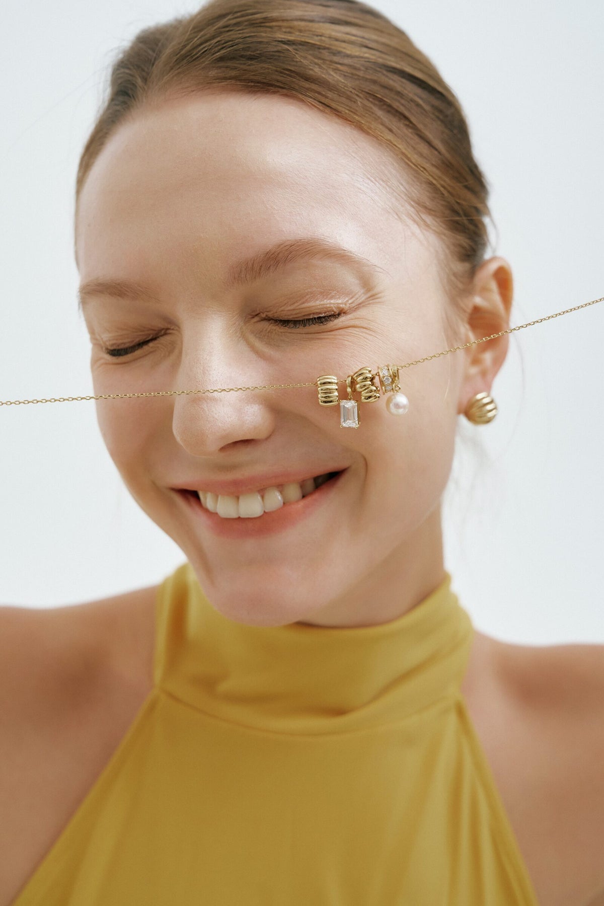 Eyes closed, laughing, the charm necklace across her cheek, the Madeleine Hoop Earrings.