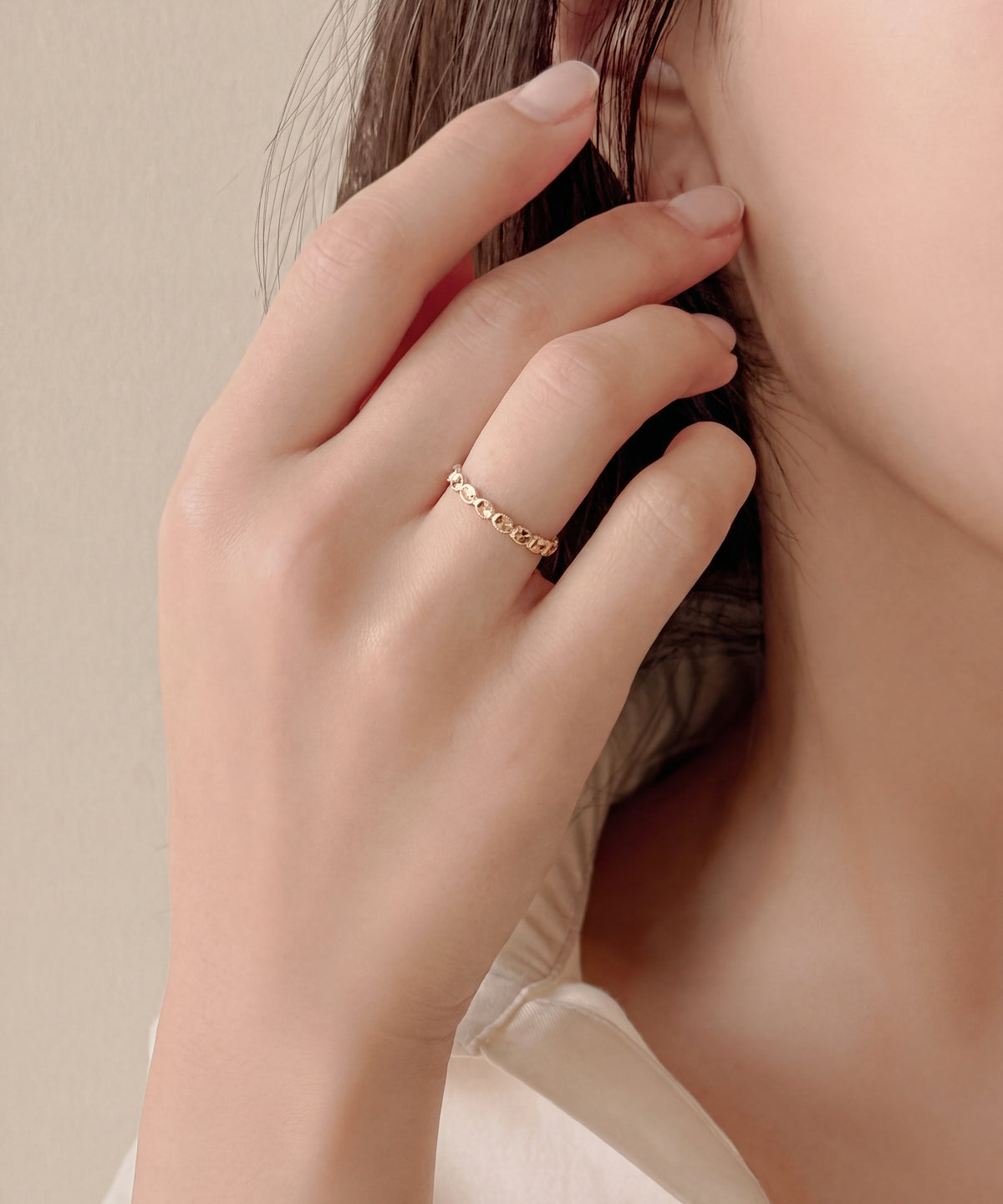 Faceted oval milgrain band worn on the finger, hand raised to the ear