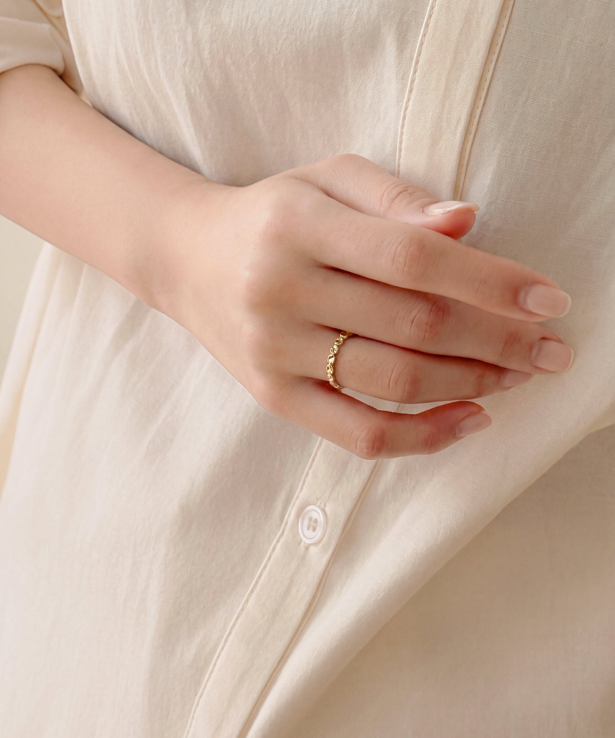 Faceted oval milgrain band worn on the finger, hand resting against a cream shirt
