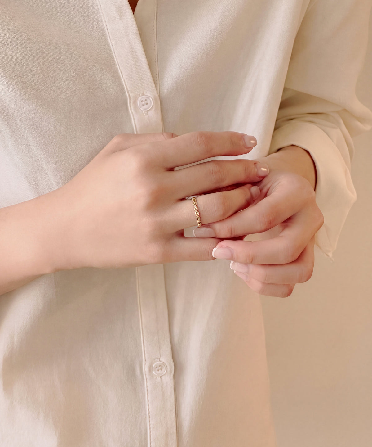 Faceted oval milgrain band worn on the finger, hands held together at a shirt front