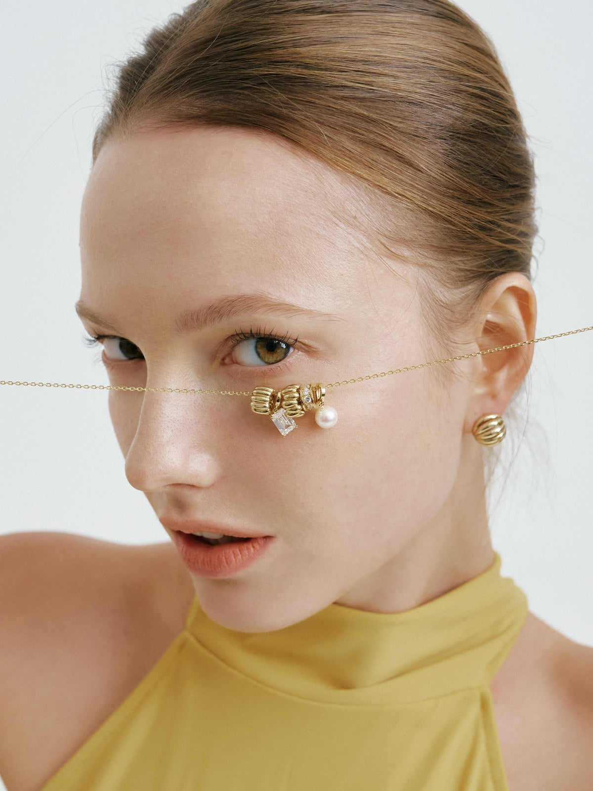 Model holding a gold chain with charms across her face