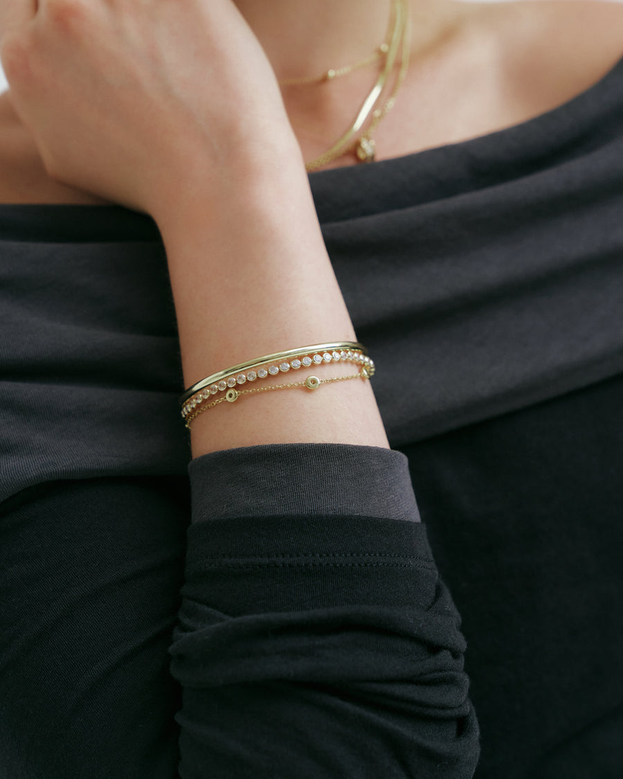 Gold bangle, tennis bracelet and station chain stacked on the wrist