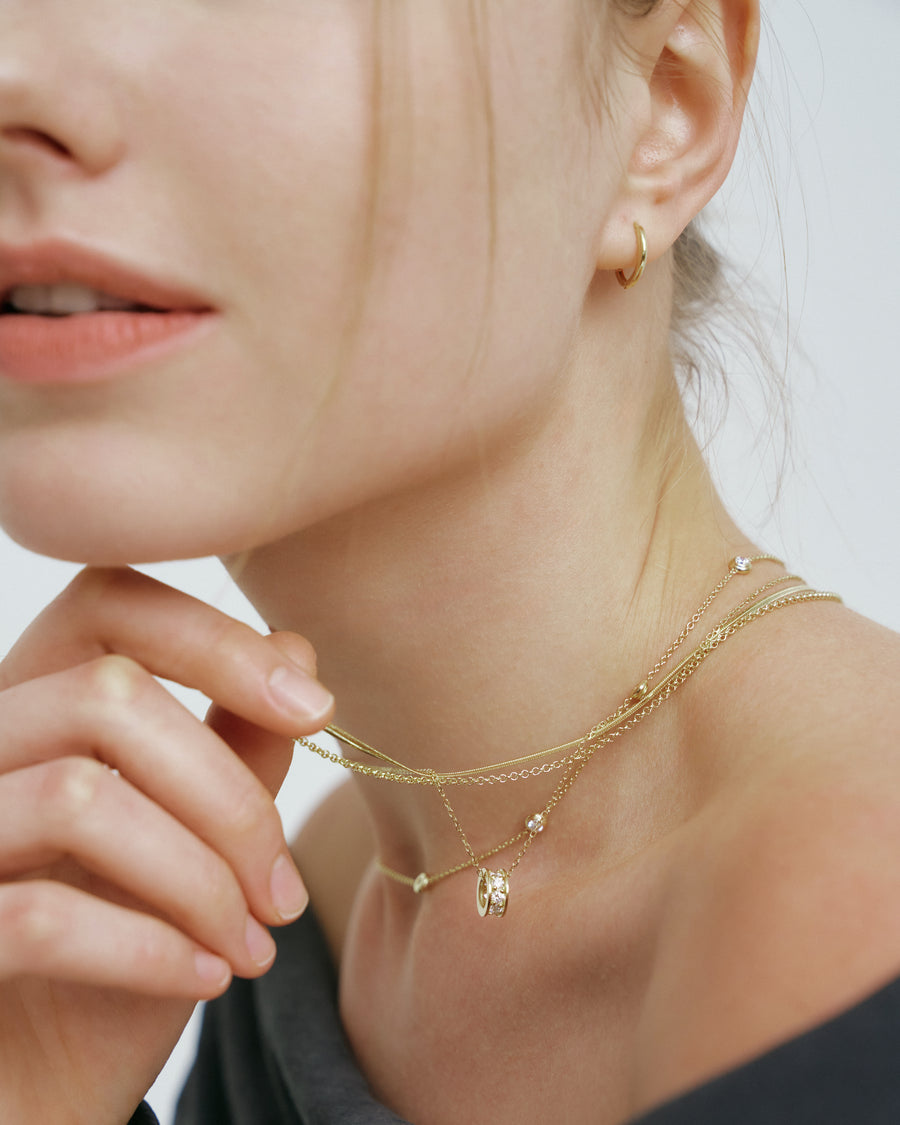 Layered gold necklaces with a diamond pendant worn above a black off-shoulder top