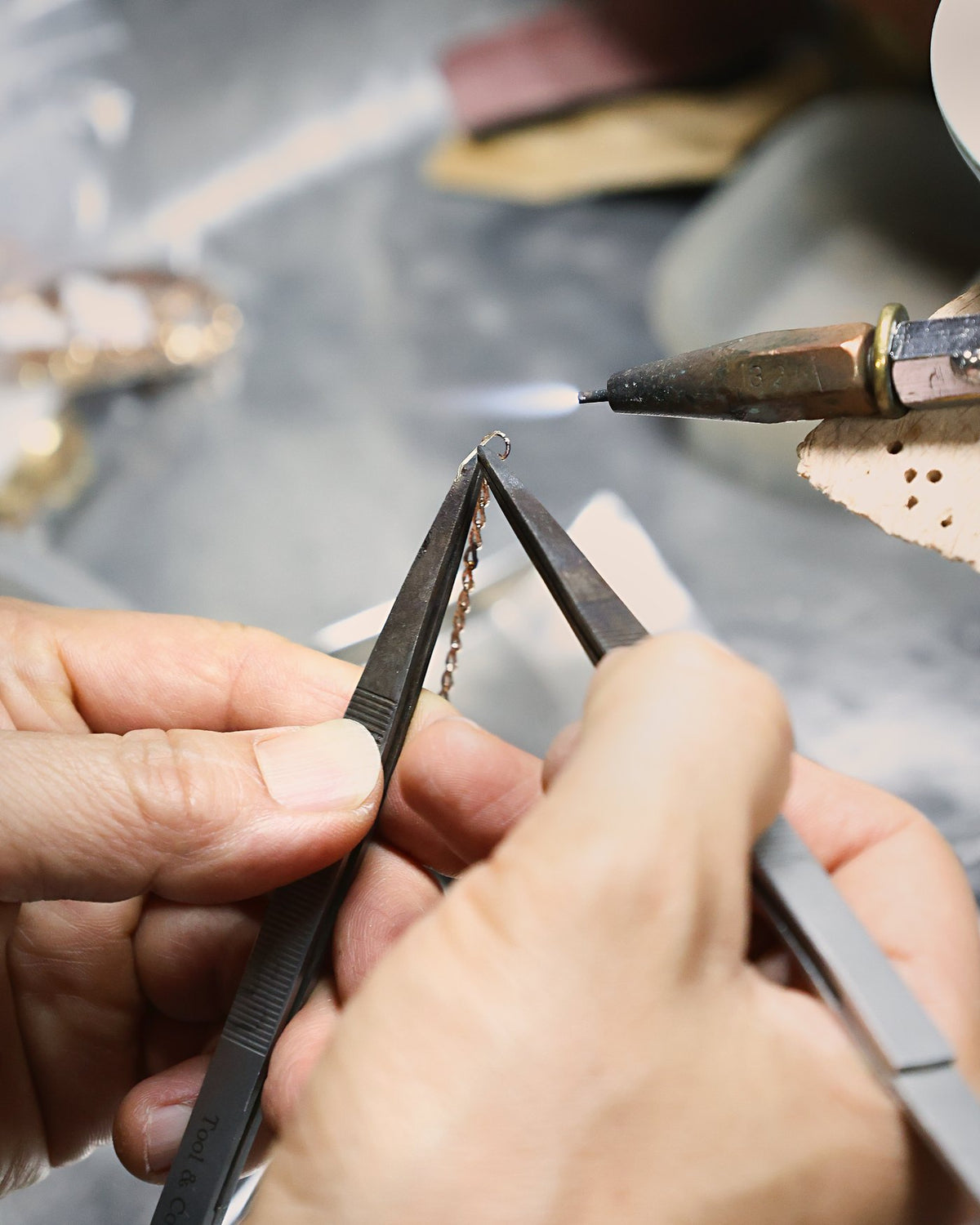 A goldsmith soldering a fine gold chain with tweezers and a torch
