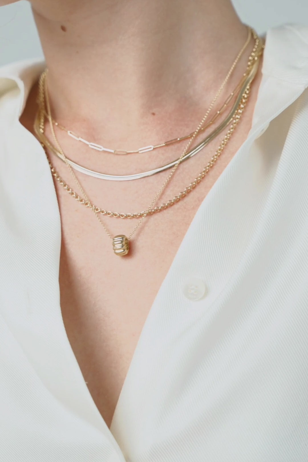 Layered gold chains on a white shirt, a gold bracelet at the wrist, and a fine chain with a small pendant