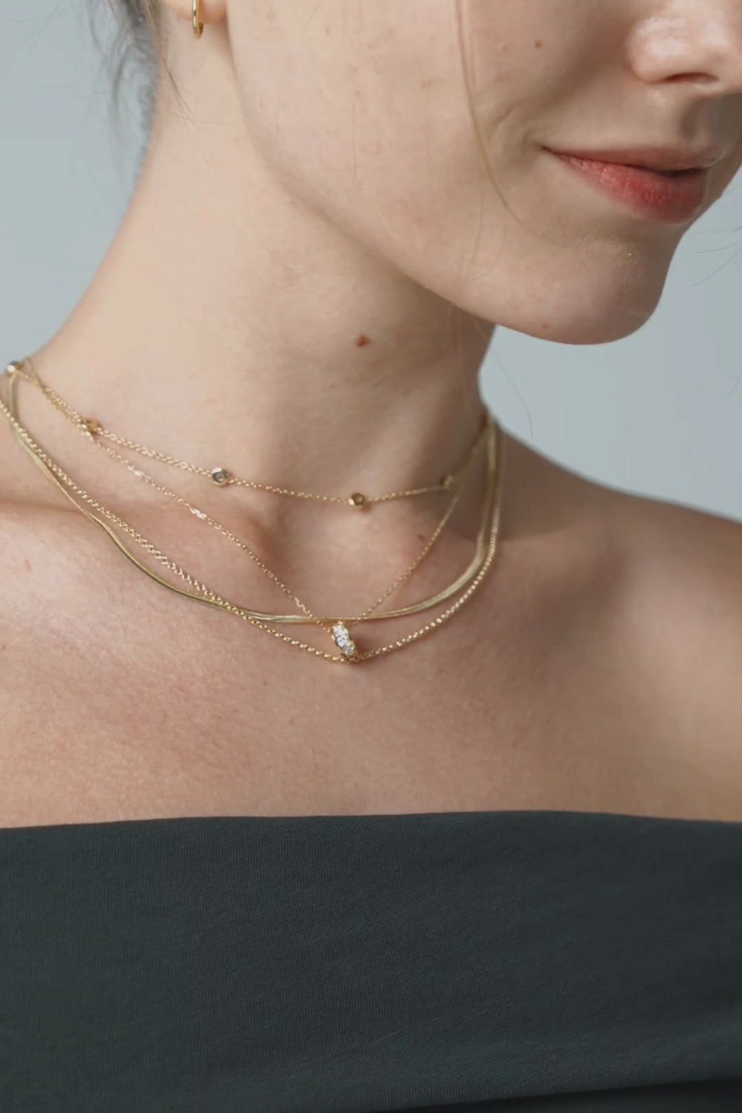Layered gold chains above a black off-the-shoulder top, then a stack of gold bracelets on a black sleeve