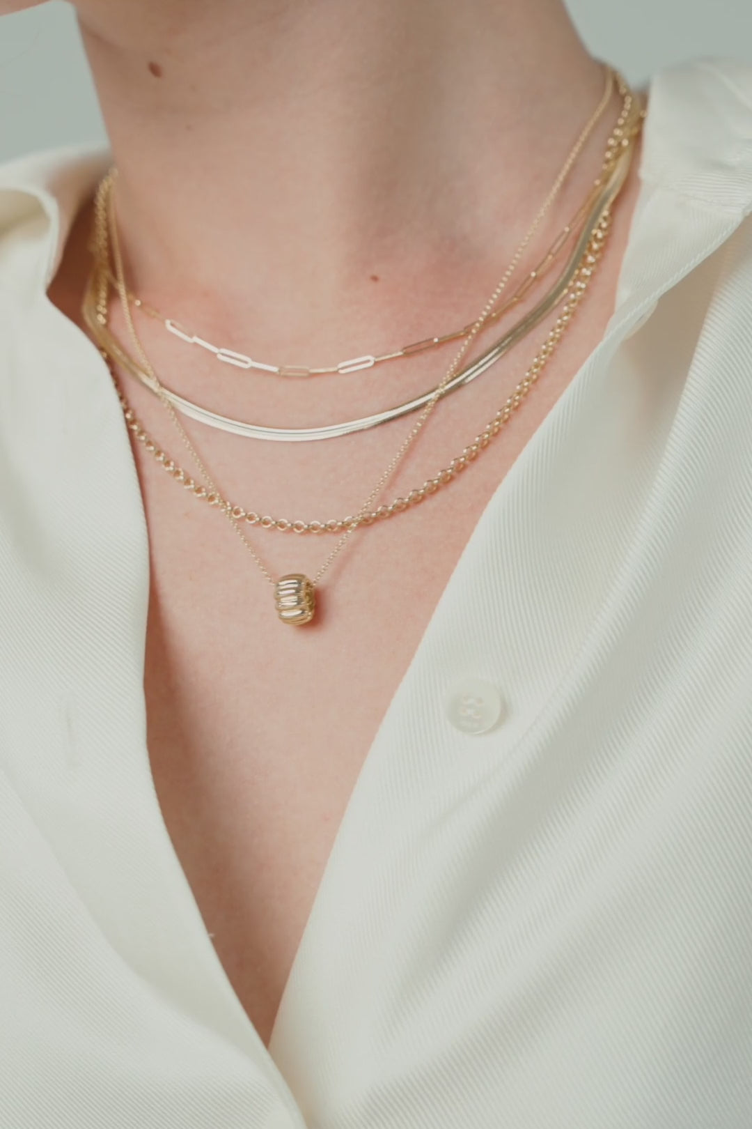 Layered gold chains on a white shirt, a gold bracelet at the wrist, and a fine chain with a small pendant