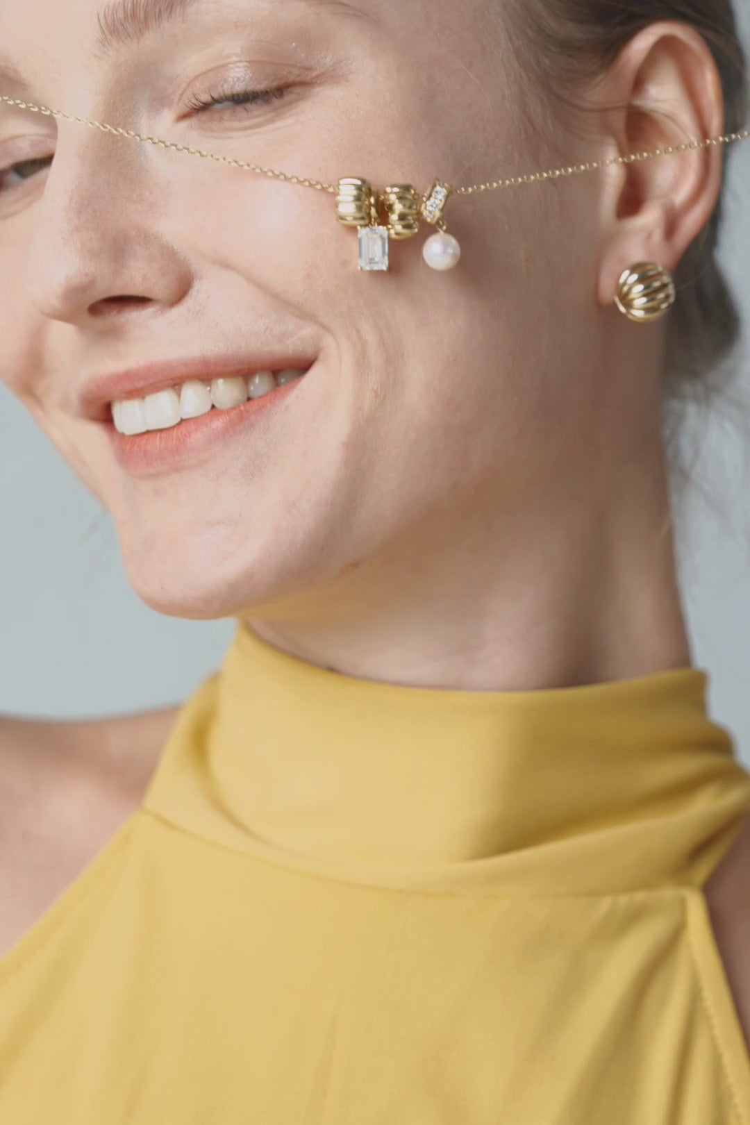 A gold bow ear charm with a pearl on a fine chain, worn with a marigold halter top