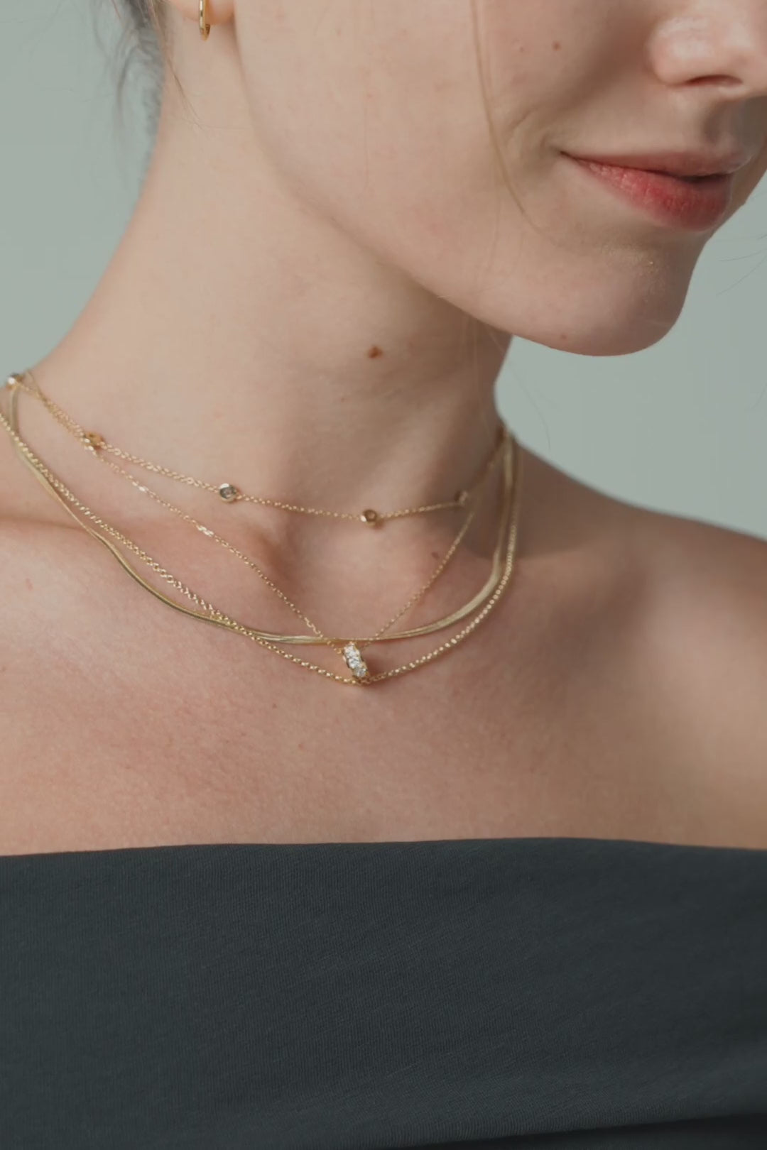 Layered gold chains above a black off-the-shoulder top, then a stack of gold bracelets on a black sleeve
