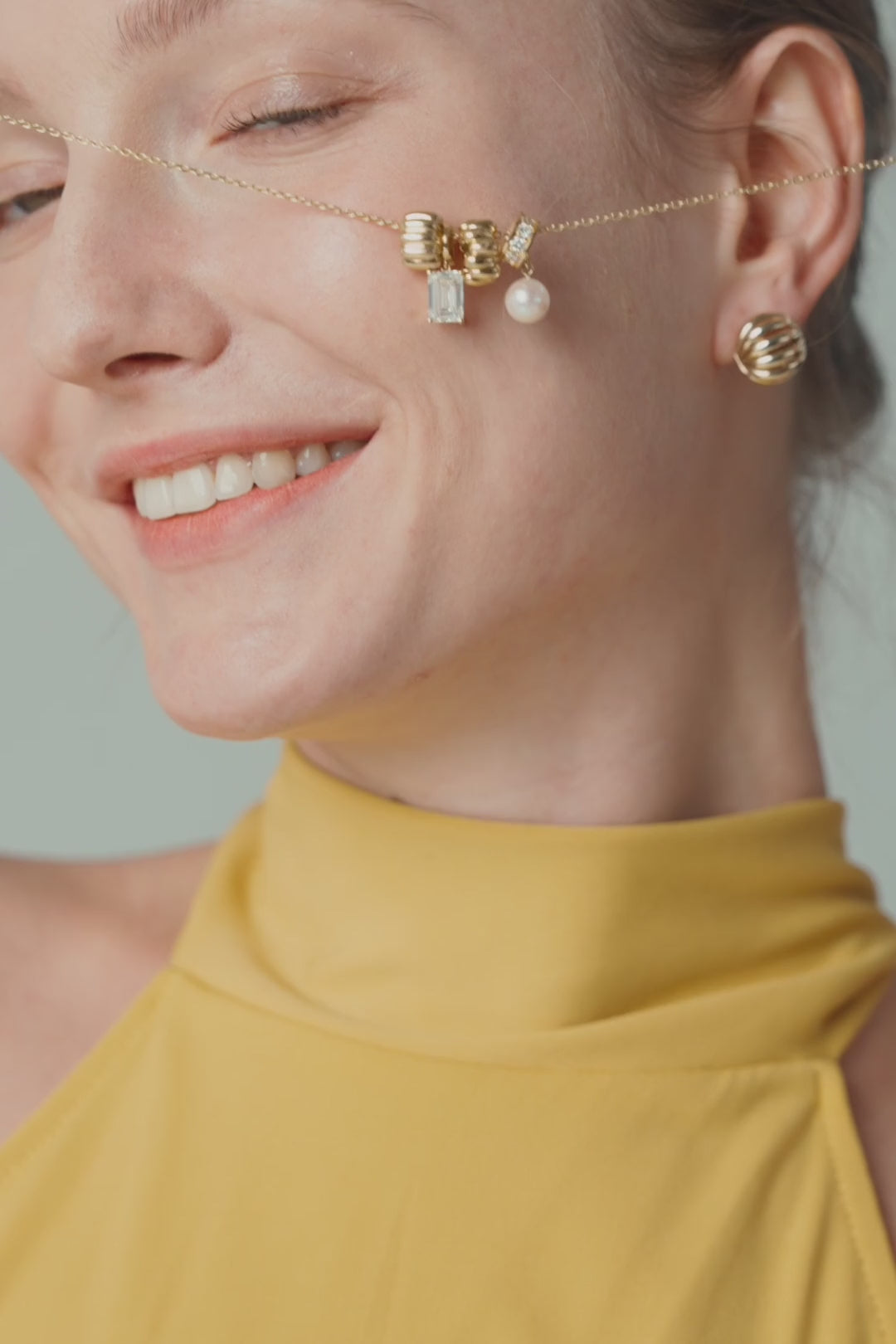 A gold bow ear charm with a pearl on a fine chain, worn with a marigold halter top